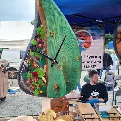 Duży zegar w kształcie liścia z zieloną żywicą, ozdobiony kwiatami na stoisku targowym